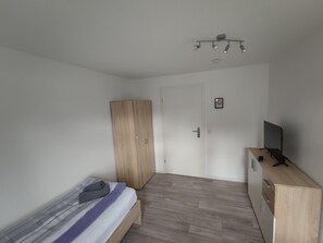 Ein Schlafzimmer mit Bett, Kleiderschrank, Schreibtisch und Fernseher sowie einer Tür.