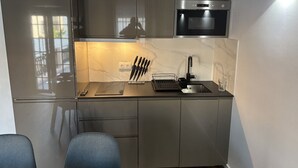 Eine kleine Küche mit Einbauofen, Spüle und Arbeitsplatte, auf der sich ein Messerblock und ein Glas befinden.