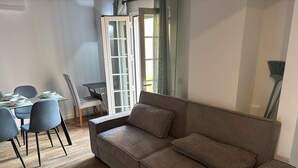 Ein Wohnzimmer mit einer Couch, Sesseln, einem Esstisch und einer Schiebetür.