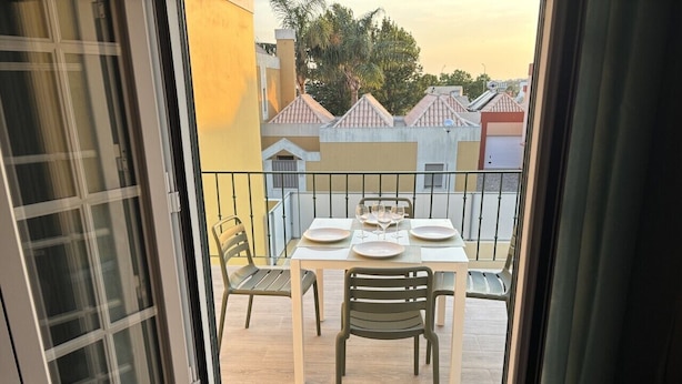 Ein Balkon im Freien mit einem Tisch für zwei Personen, Stühlen und Blick auf Gebäude im Hintergrund.
