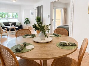 Une table de salle à manger ronde, agrémentée d’un vase blanc servant de centre de table, et entourée de six chaises en osier.