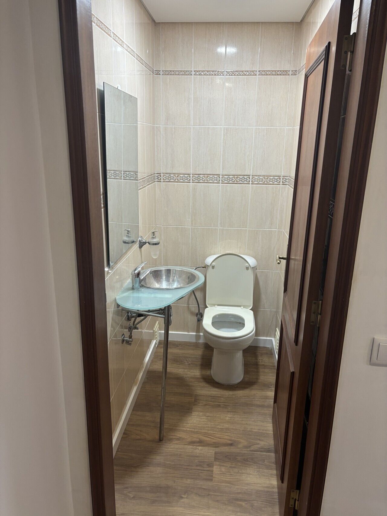 A bathroom with a glass sink, a toilet, and a shower area.
