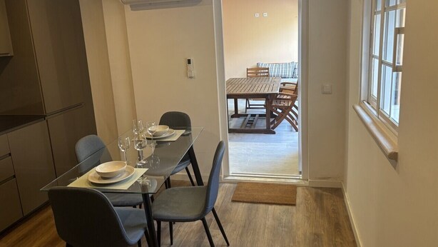 Un coin repas avec une table dressée pour quatre personnes, une cuisine équipée de meubles modernes et une vue sur une salle à manger avec une table et des chaises en bois.
