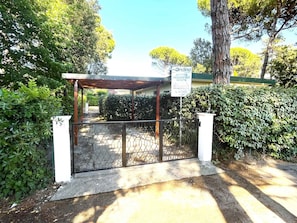 Ein begrenzter Eingangsbereich mit einer Pergola, umgeben von Grünpflanzen und blauem Himmel.