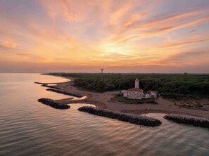 A coastal scene with a lighthouse, a beach, and a rocky breakwater. - Holiday apartment with air conditioning and garden (Bibione)