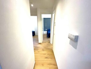 Ein Korridor mit Holzboden, weißen Wänden und einer blauen Tür am Ende.