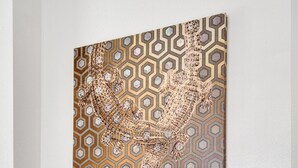 Un'opera d'arte appesa al muro con un motivo geometrico, un tavolino consolle con piano in vetro e una ciotola decorativa, e una presa elettrica sulla parete.