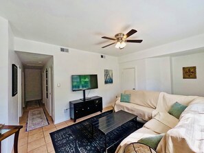 Ein Wohnzimmer mit Flachbildfernseher, Deckenventilator, Sofa und Couchtisch.