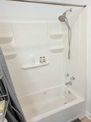 Eine weiße Badewanne mit Duschbrause und Ablagefläche für Toilettenartikel.