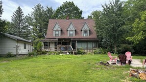 Ein Haus mit Veranda, Rasen und einer Terrasse mit Adirondack-Stühlen.