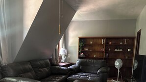 Ein Wohnzimmer mit einem Ecksofa, einem Couchtisch, Holzboden, Deckenventilator und einer Bücherwand.
