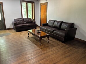 A living room with two leather sofas, a wooden coffee table, and a large window with blinds. - 8 Acres of Privacy  Your Group Escape (Rockford)