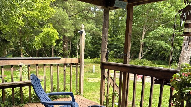 Eine Holzterrasse mit zwei blauen Adirondack-Stühlen und einem kleinen Tisch, umgeben von einem Holgitter mit Blick auf eine grüne Landschaft.