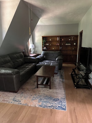 A living room with a sectional sofa, a coffee table, a bookshelf, and a TV stand.