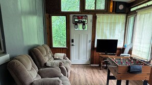 Ein Zimmer mit einer Couch, einem Kicker, einem Fernseher und einer Tür mit einem Fenster.
