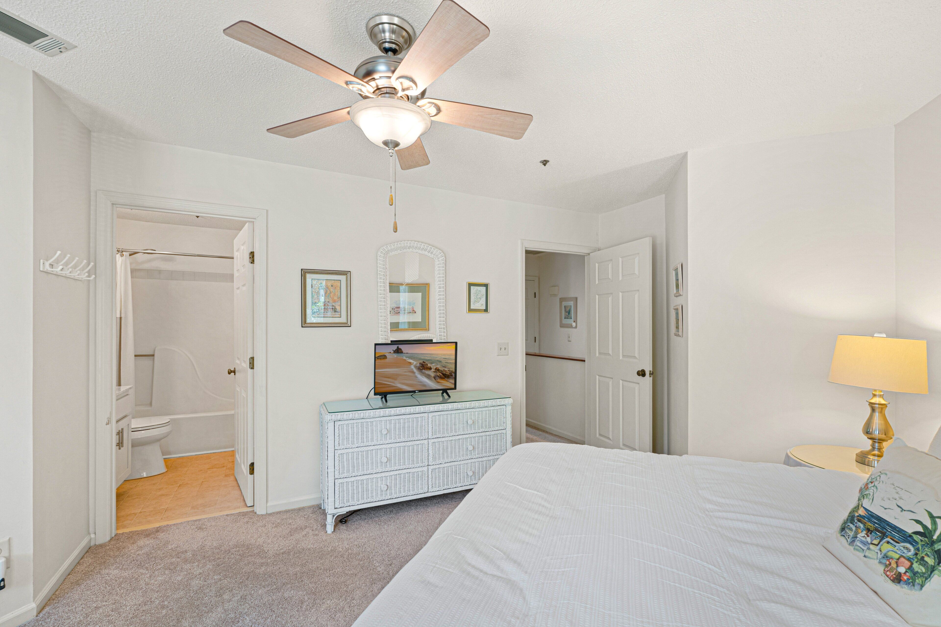 A bedroom with a bed, a dresser, a ceiling fan, a TV, and a bathroom with a toilet and shower.