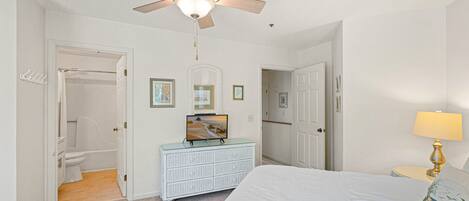 A bedroom with a bed, a dresser, a ceiling fan, a TV, and a bathroom with a toilet and shower.