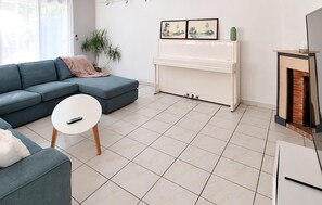 Ein Wohnzimmer mit Ecksofa, einem weißen Klavier, einem kleinen runden Tisch und einem Kamin.