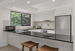 Eine moderne Küche mit weißen Schränken, einem Edelstahlkühlschrank, einer schwarzen Arbeitsplatte und einem Fenster mit Blick auf Bäume.