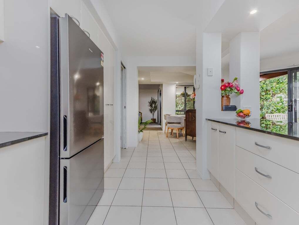 A modern kitchen with white cabinetry, a stainless steel refrigerator, and a dining area with a table and chairs.