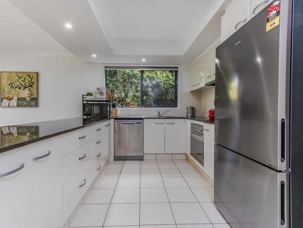 A modern kitchen with white cabinetry, stainless steel appliances, and a window providing natural light.