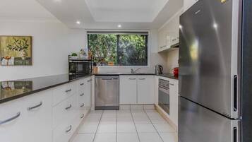 A modern kitchen with white cabinetry, stainless steel appliances, and a window providing natural light.