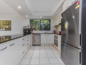 Una cocina moderna con armarios blancos, electrodomésticos de acero inoxidable y un ventanal que proporciona luz natural.