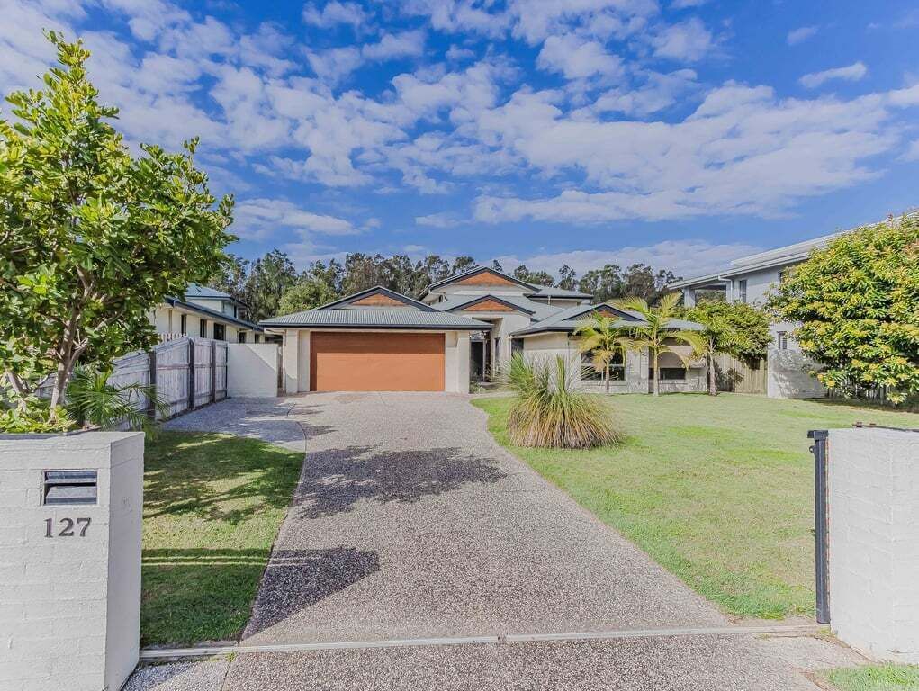 A residential property with a driveway leading to a garage, surrounded by a well-maintained lawn and mature trees.