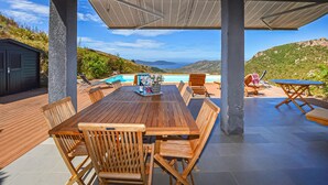 An outdoor patio with a wooden table and chairs, a pool, and a view of the hills. - Lovely home in Appietto (Appietto)