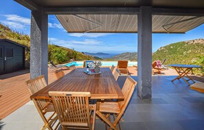 Eine Terrasse im Freien mit Holztisch und -stühlen, einem Pool und Blick auf die Hügel.