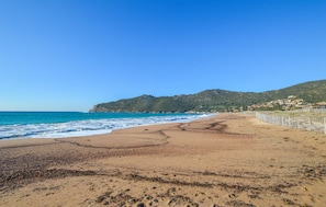 Ein Strand mit blauem Himmel, Wellen und einer fernen Hügelkette mit Gebäuden.