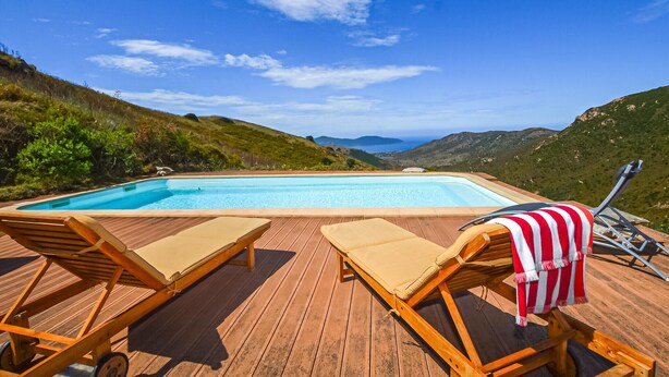 A wooden deck with a pool, two lounge chairs, and a view of mountains and the sea. - Lovely home in Appietto (Appietto)