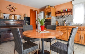 A kitchen with a round wooden table, four wicker chairs, a red potted plant, and wooden cabinets. - Nice home in MEZZAVIA with outdoor swimming pool (MEZZAVIA)