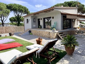 Una villa moderna con patio, mobiliario exterior y un muro de piedra.