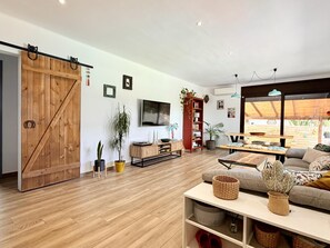 Amplia sala de estar con una puerta corrediza de estilo rústico, piso de madera, un sofá, un televisor y un comedor con una mesa y sillas.