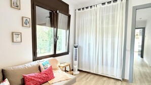 Ein Wohnzimmer mit einer Couch, einem Standheizkörper, einem Fenster mit Jalousien und einer Tür zu einem anderen Raum.