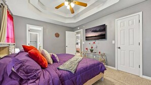 Ein Schlafzimmer mit einem Bett, einem Deckenventilator, einem Fernseher und einer Tür.
