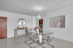 A modern dining area with a glass table and chairs, a round mirror, a wooden cabinet, and a painting on the wall. - Family & Friends Beach GetawayHollywood Beach- 2BR/2BA (Hollywood)