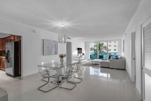A modern kitchen with stainless steel appliances, a glass dining table with chairs, and a large window offering a view of palm trees and buildings. - Family & Friends Beach GetawayHollywood Beach- 2BR/2BA (Hollywood)