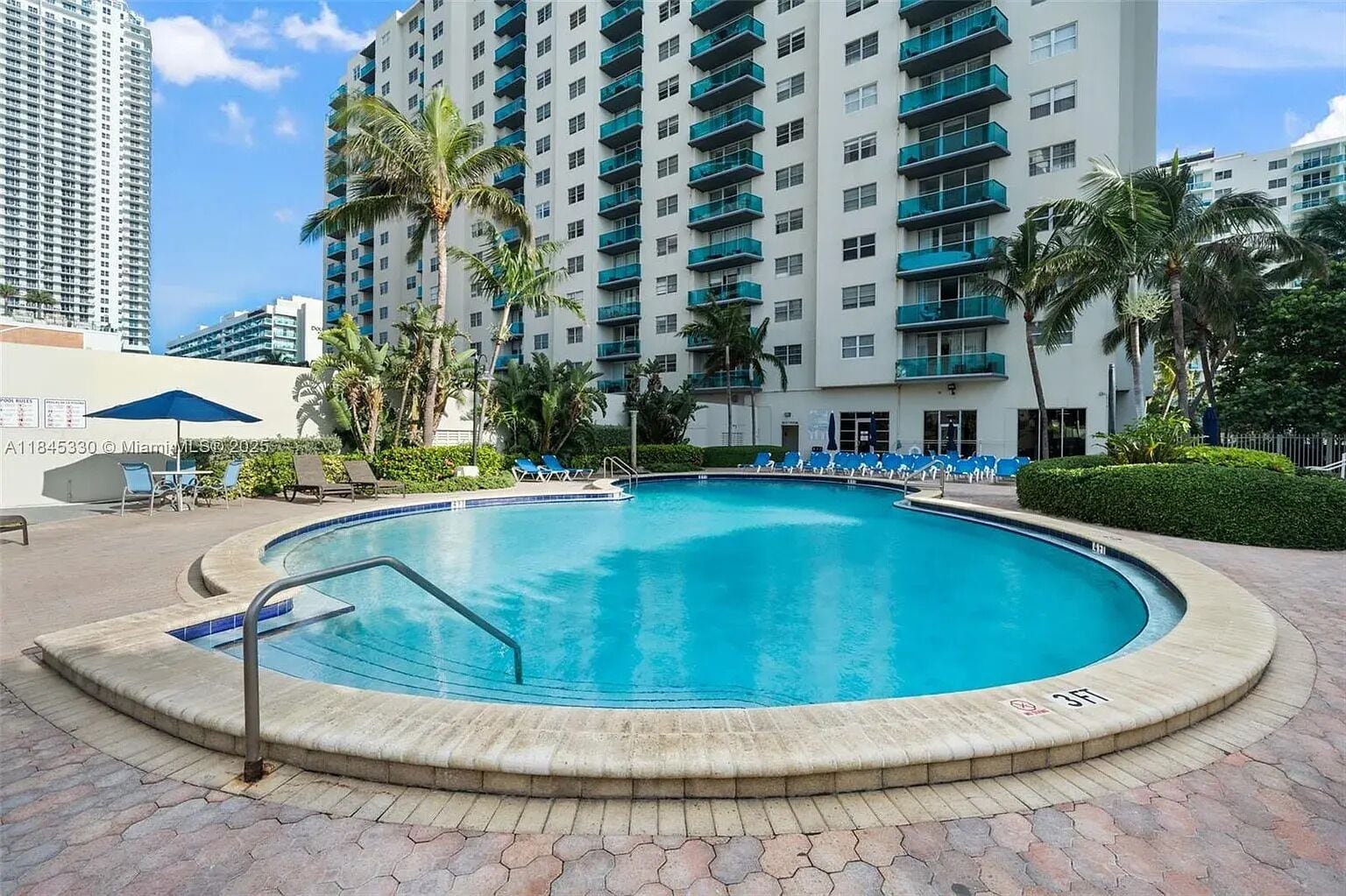 A swimming pool with a 3ft depth marker, surrounded by lounge chairs and palm trees, with a high-rise building in the background.
