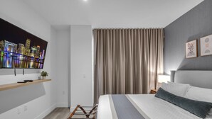 Una habitación de hotel moderna con una cama, un televisor montado en la pared, un estante de madera y una ventana con cortinas.