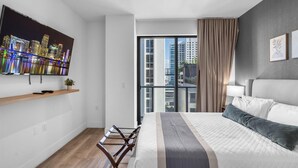 Una habitación de hotel moderna con una cama grande, un televisor en la pared, un balcón con vistas a la ciudad y un escritorio con una planta.