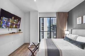 Ein modernes Hotelzimmer mit einem großen Bett, einem Wandfernseher, einem Balkon mit Stadtblick und einem Schreibtisch mit Pflanze.