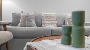 Una sala de estar moderna con un sofá gris, cojines estampados y una mesa de centro de madera con velas.