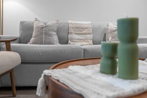 Ein modernes Wohnzimmer mit einem grauen Sofa, gemusterten Kissen und einem Holztisch mit Kerzen.
