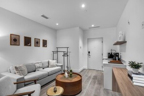 A modern living room with a grey sofa, a wooden coffee table, and a kitchen area with a microwave and a sink. - Bright & Modern Brickell Retreat-Prime Location- 7th Floor (Miami)