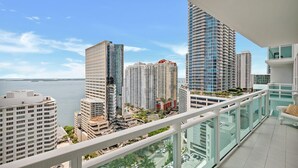 Un edificio de gran altura con un diseño arquitectónico moderno, un balcón con baranda de vidrio y vistas a la ciudad y al agua.