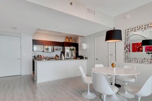 A modern kitchen with built-in appliances, a central island with seating, and a dining area with white chairs and a table. - High-Floor Bay View Retreat at The Plaza Brickell (Miami)