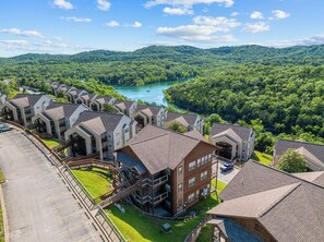 A residential area with multiple two-story houses, a parking lot, and a river in the background. - Condo Mins to Silver Dollar City w Free Tickets_Outdoor Pool_Tennis Courts_Water Path (Branson)
