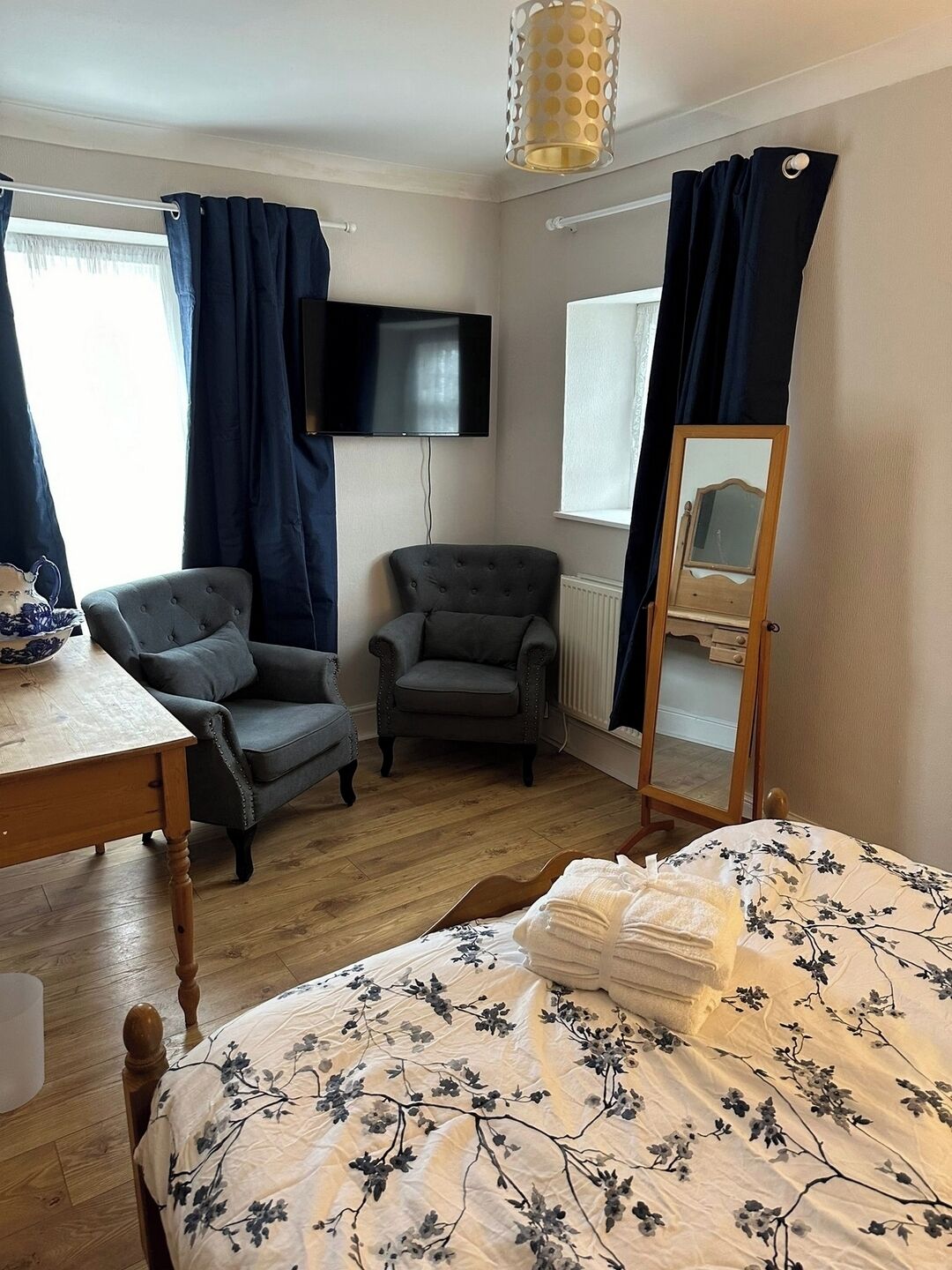 A room with a bed, two armchairs, a table, a TV, a mirror, and a window with curtains.